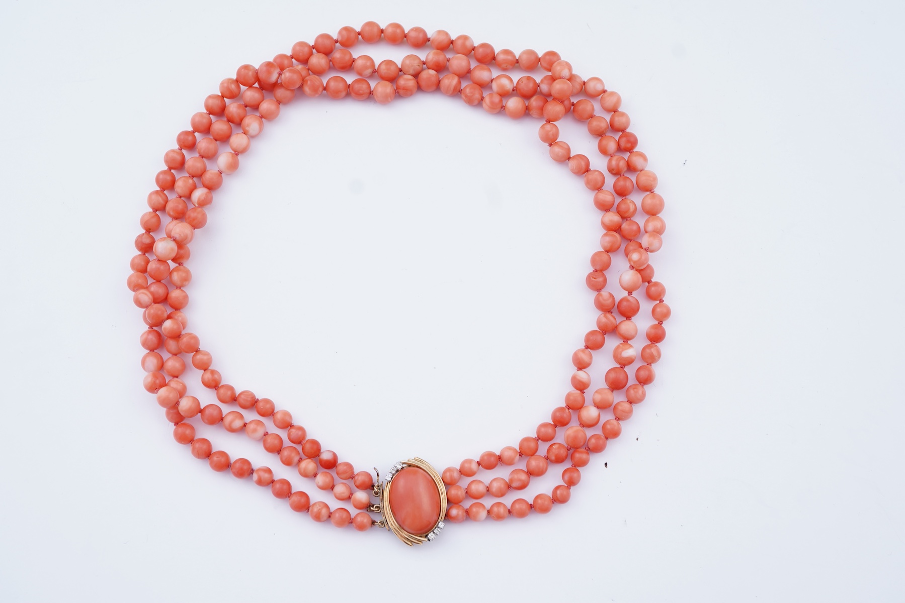 A coral necklace, composed of three strands of coral beads measuring approximately 5.1-6.6mm diameter, to a gold clasp set with a coral cabochon and brilliant-cut diamonds, mounted in gold, length 45.5cm, stamped 14K, ca